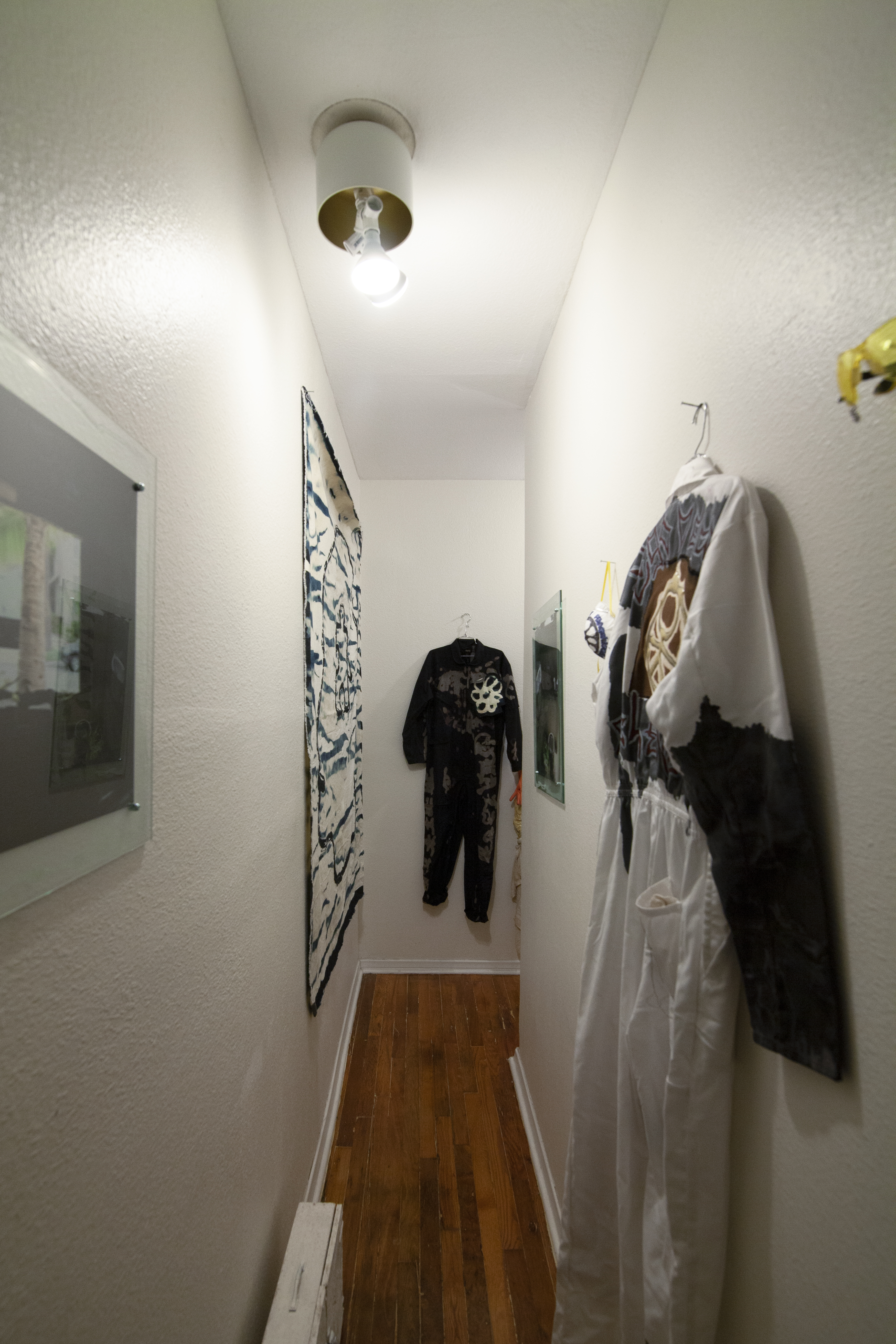 A narrow hallway with jumpsuits, photo prints and artworks hung on white walls